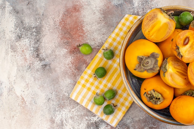 Top view delicious persimmons in a bowl yellow kitchen towel feykhoas on nude background