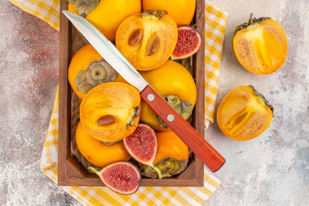 Top view delicious persimmons cut figs and a knife in wood box on nude background