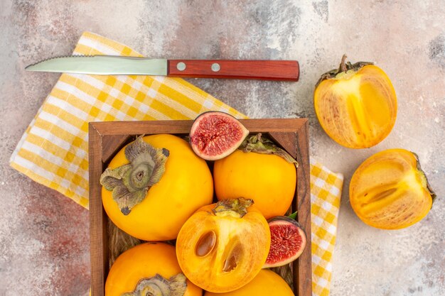 Top view delicious persimmons and cut figs in wood box on nude background