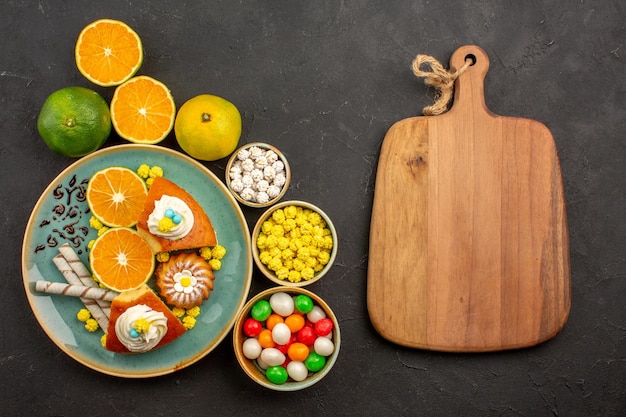 Free photo top view delicious pie slices with candies and fresh tangerines on dark background fruit cake sweet biscuit pie