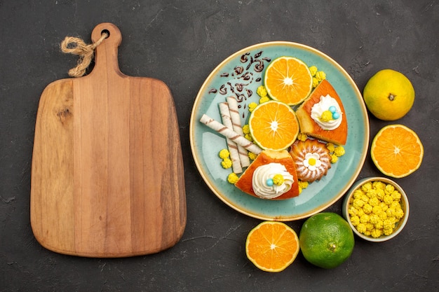 Free photo top view delicious pie slices with pipe cookies and fresh sliced tangerines on the dark background fruit cake pie sweet biscuit