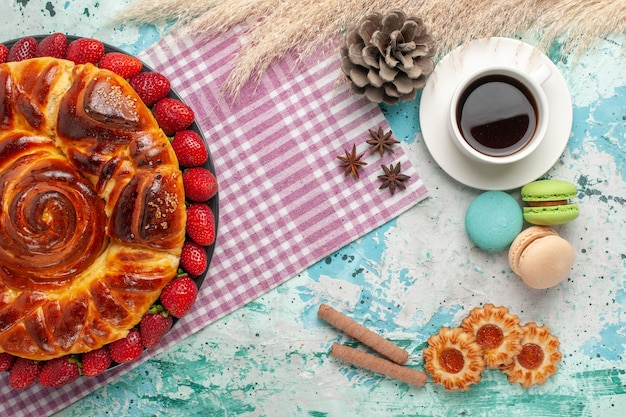 Top view delicious pie with fresh red strawberries macarons and cup of tea on blue surface