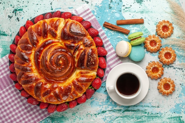 Top view delicious pie with fresh red strawberries macarons and cup of tea on blue surface