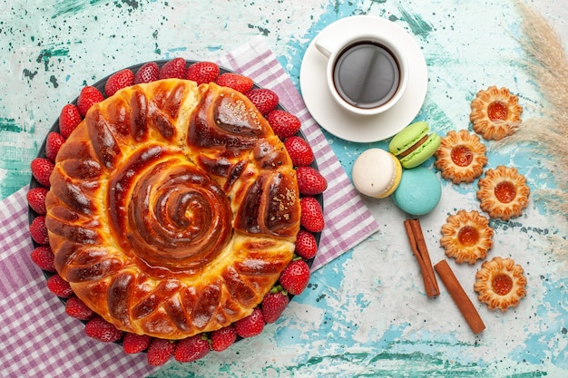 Top view delicious pie with strawberries macarons and cup of tea on the blue surface