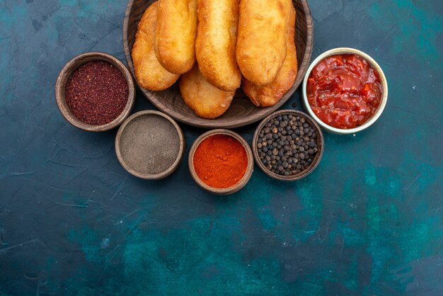 Top view delicious pies with meat filling along with seasonings on dark-blue desk dough pie bread bun food