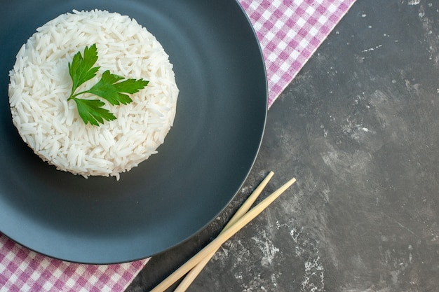 Top view of delicious rice meal served with green on a black plate on purple stripped towel and wooden chopstics on the right side on dark background