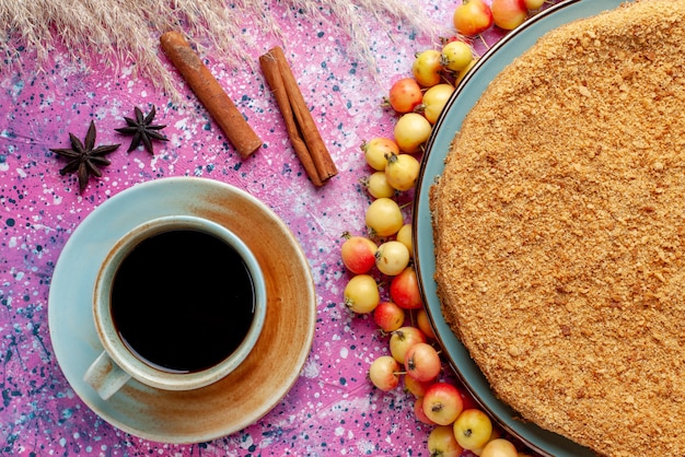 Top view delicious round cake inside plate with lined sweet cherries tea and cinnamon on the bright pink desk cake pie biscuit