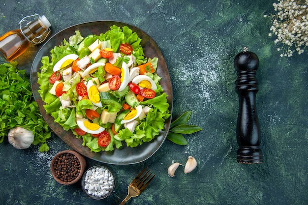 Top view of delicious salad with many fresh ingredients spices garlics fallen oil bottle flower on black green mix colors background