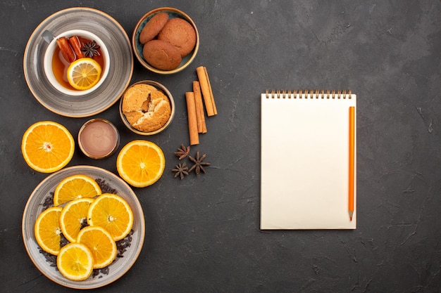 Top view delicious sand cookies with fresh sliced oranges and cup of tea on dark desk sugar biscuit sweet cookie fruit