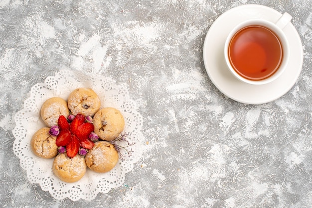 Free photo top view of delicious sand cookies with fresh strawberries and cup of tea on white surface