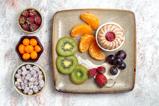 Top view delicious sliced fruits with cake and candies on white background fruit fresh tea candy cake biscuit