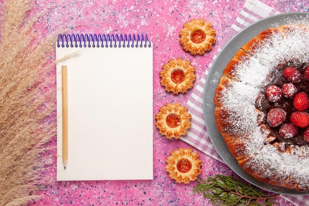 Top view delicious strawberry cake with notepad and  on light-pink surface