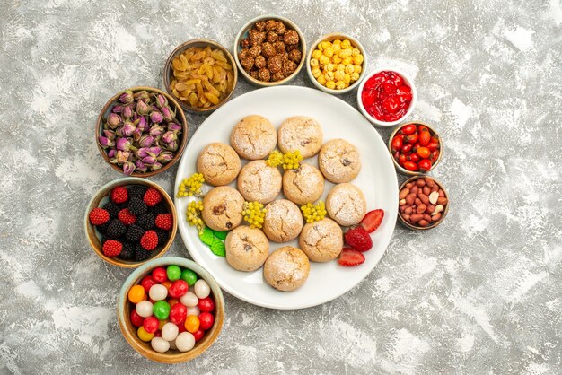 Top view delicious sugar cookies inside plate with different nuts and candies on white background sugar cookie sweet biscuit cake tea