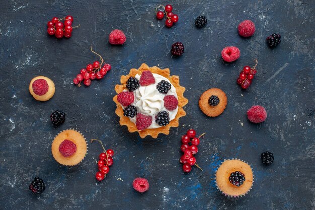 Top view of delicious sweet cake with different berries and yummy cream along with cranberries spread on dark desk, fruit berry cake biscuit sweet