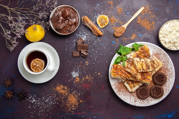 Top view delicious sweet pastries with chocolate cookies and cup of tea on dark space