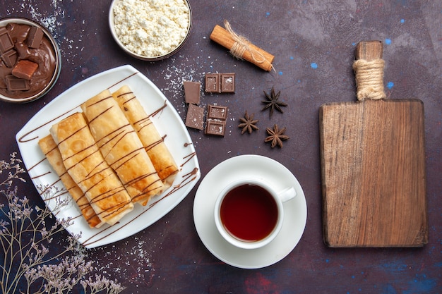 Top view delicious sweet pastries with chocolate and cup of tea on dark desk