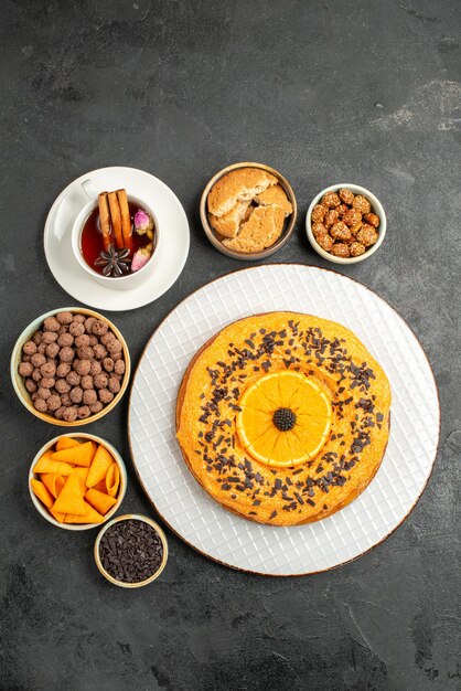 Top view delicious sweet pie with orange slices and cup of tea on dark surface cookies pie biscuit dessert tea cake