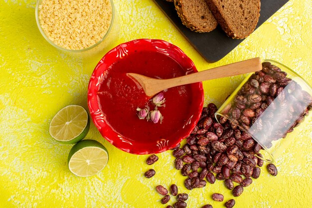 Top view delicious tomato sauce with dark bread loafs lemon and raw beans on yellow desk soup food meal dinner