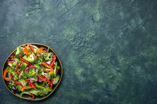 Free photo top view of delicious vegan salad in a plate with various fresh vegetables on the right side on dark background