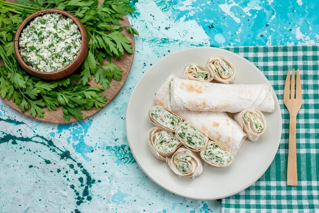 Top view of delicious vegetable rolls whole and sliced with greens and salad on blue desk, food meal roll vegetable snack