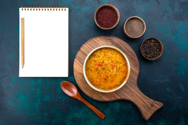 Top view delicious vegetable soup inside round plate with seasonings on the dark-blue desk.