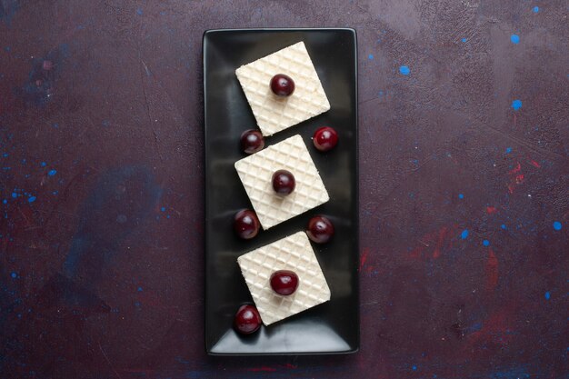 Top view of delicious waffles with cherries inside plate on the dark surface