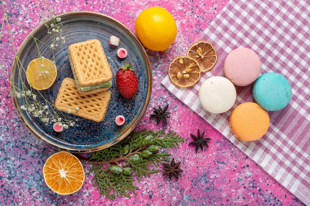 Top view of delicious waffles with french macarons on the light-pink desk