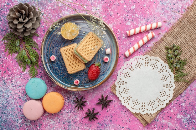 Top view of delicious waffles with french macarons on pink desk