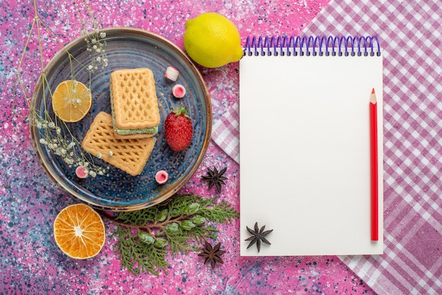 Top view of delicious waffles with notepad on the light-pink surface