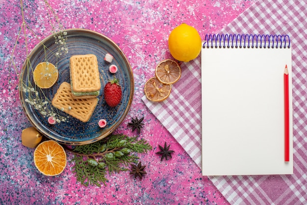 Top view of delicious waffles with notepad on pink surface