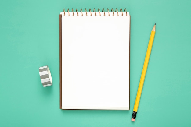 Top view desk arrangement with empty notepad on blue background