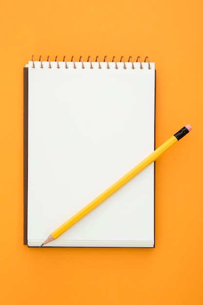 Top view desk arrangement with empty notepad on orange background