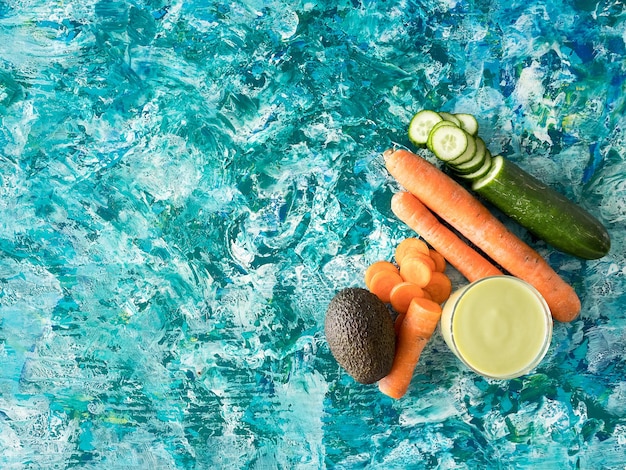 Top view of detox juice next to carrots, cucumber and avocado on colorful wooden background