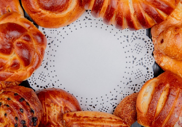 Top view of different bakery products set in round shape around doily paper as background