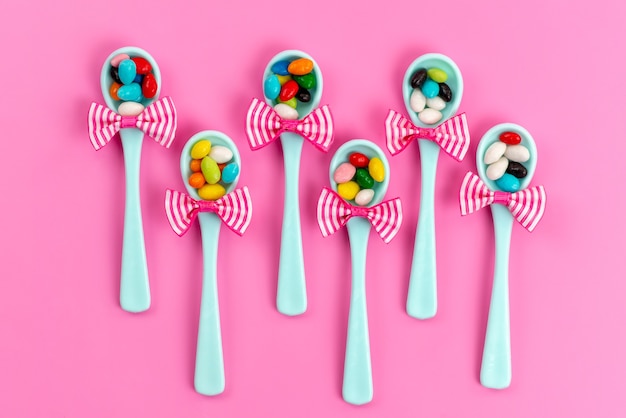 Free photo a top view different colored candies inside green spoons with bow on pink, sweet rainbow sugar