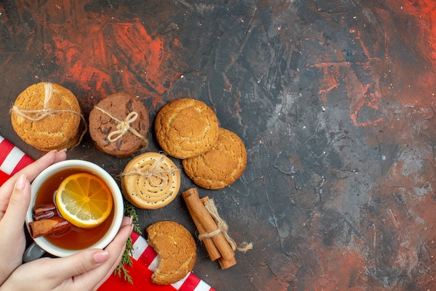 Free photo top view different cookies cup of tea cinnamon sticks on dark red table free space