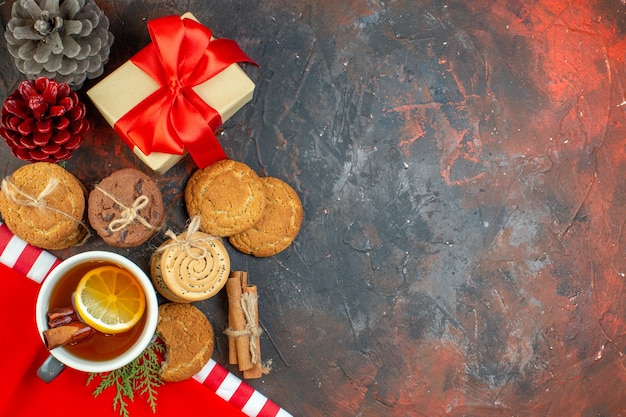 Top view different cookies tied with rope cup of tea pinecones cinnamon sticks on dark red table with copy place