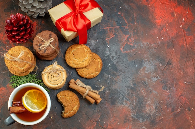 Top view different cookies tied with rope cup of tea pinecones gift on dark red table with copy place