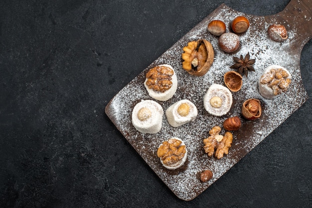 Top view different cookies with cakes and walnuts on the dark-grey surface