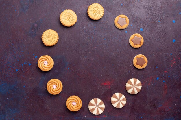 Top view different cookies with cream inside on dark surface