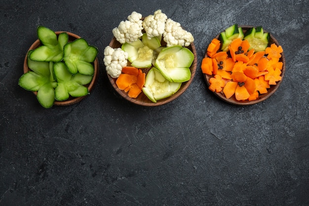 Top view different designed vegetables inside pots on dark-grey space