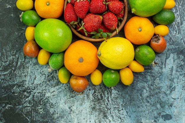 Top view different fresh fruits with red strawberries on grey background