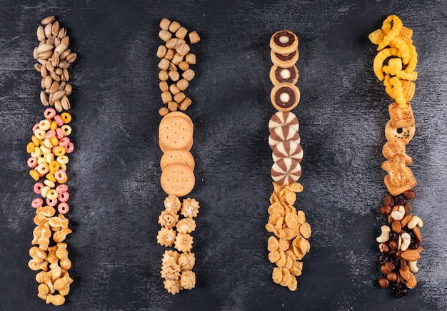 Free photo top view of different kind of snacks as nuts, crackers and cookies with copy space on dark surface horizontal