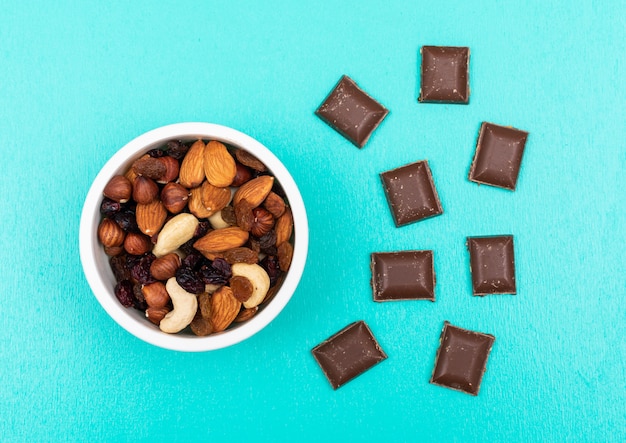 Free Photo top view of different kind of snacks as nuts with dried fruits in bowl and chocolate on blue surface horizontal