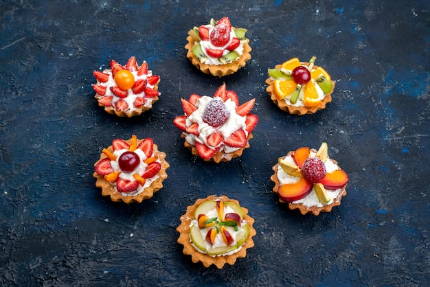 A top view different little cakes with cream and fresh sliced fruits on the blue backgound fruit cake biscuit