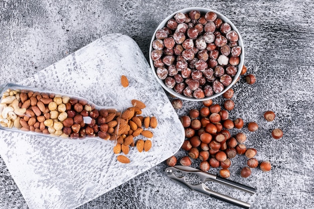 Top view different nuts in full bottle of nuts and bowl with nutcracker and pecan, pistachios, almond, peanut, cashew, pine nuts