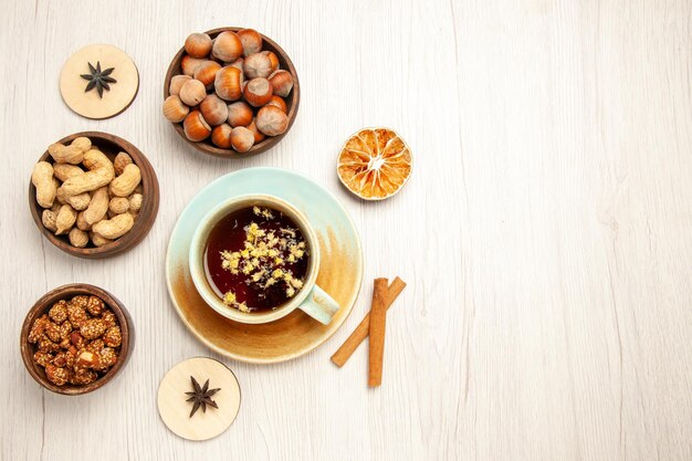 Top view different nuts inside little pots with cup of tea on white desk nuts snack walnut hazelnut