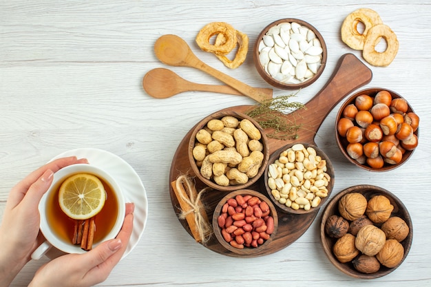 Top view different nuts peanuts hazelnuts and walnuts with cup of tea on white table