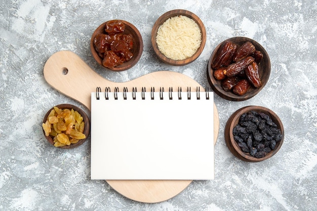 Top view different raisins inside little pots with notepad on white space