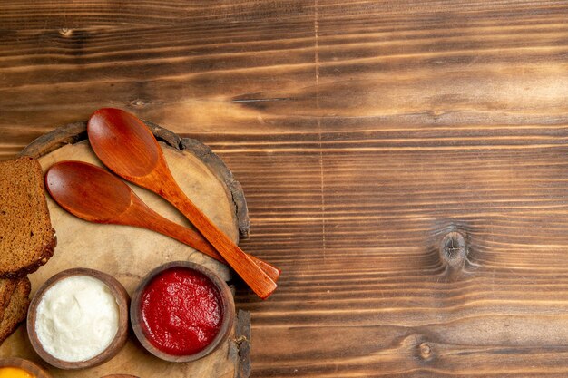 Top view of different seasonings with black bread loafs on brown table